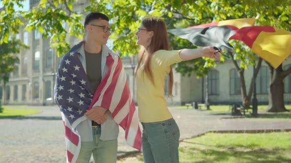 Portrait of Happy American Male Student Wrapped in National Flag Standing with Smiling Beautiful alt