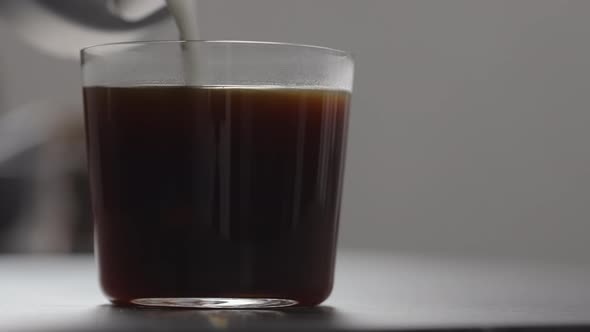 Slow Motion Pour Cream in Coffee in Tumbler Glass on Concrete Countertop with Copy Space alt