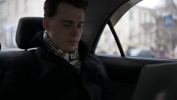 Attractive Young Male is Riding in a Car with Laptop Opened on His Laps alt