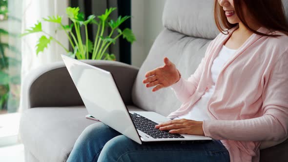 Young woman greeting in a video call and sitting on sofa in the living room at home