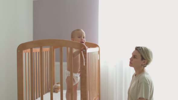 Mother Trying Calm Screaming Crying Baby Toddler Infant in Crib Put to Bed Cot alt