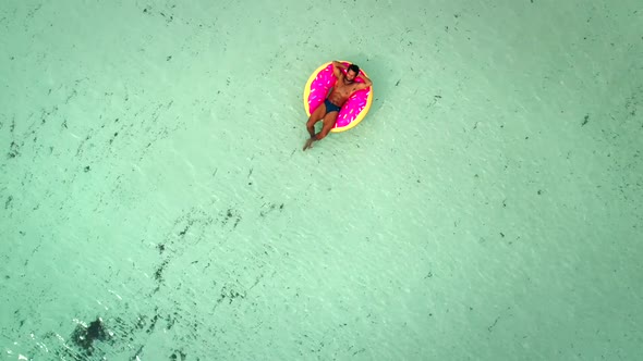 Aerial view of man floating on inflatable donut mattress, relaxing. alt
