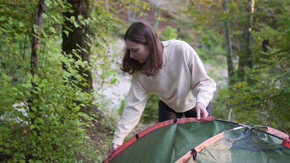 A Young Woman Sets Up a Tent in the Woods