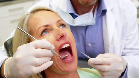Dentist examining a female patient with dental tools alt