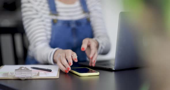 Woman sitting at desk taking smartphone, close-up alt