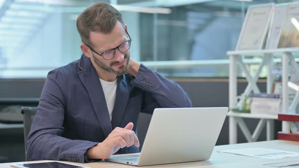 Middle Aged Businessman Having Neck Pain While Using Laptop in Office alt