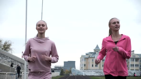 Identical Caucasian Twin Sisters in Pink Sportswear Running Outdoors Together