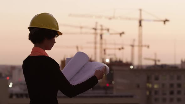 Architect holding plans looking at construction site at sunset