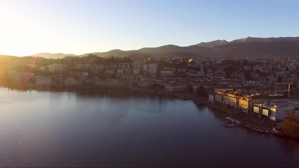 A drone view of a city surrounded by mountains, next to a lake, during a sunset in autumn. Lugano, T alt