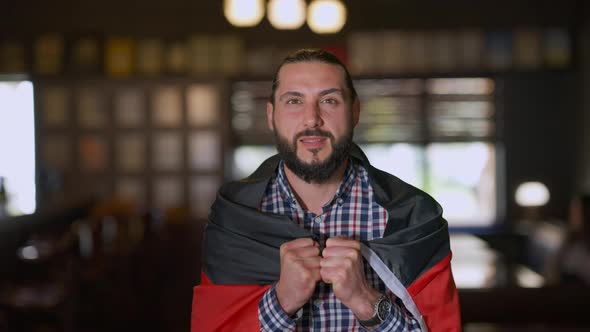TV POV of Excited Sport Fan Rejoicing Victory with German Flag Standing in Pub Indoors alt