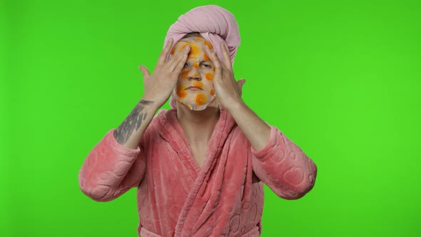 Portrait of Transsexual Man in Bathrobe Looking in Mirror Wearing Face Mask alt