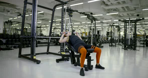 Sporty Girl in the Gym Doing Sitting Leaning Back Exercise with Dumbbells in Hand, Then Zamanivaet alt