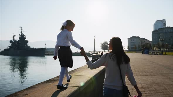 A girl in school uniform is walking on the railing of the promenade with mother. alt