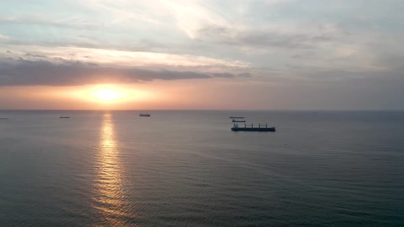 A drone flight around container ships into the sea at sunrise alt