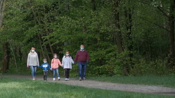 A Family in Medical Masks Walks in the Park in the Spring. Father and Mother Carry Children in Their