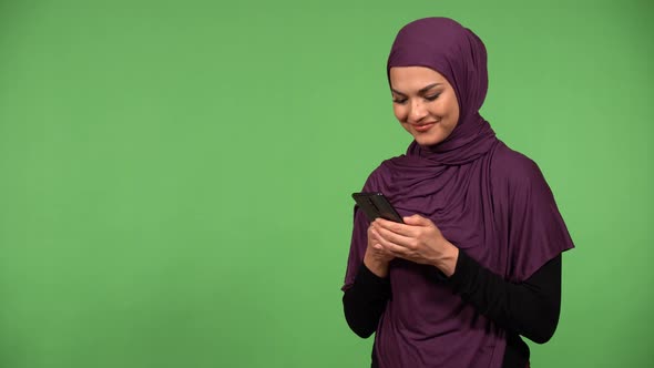 A Young Beautiful Muslim Woman Works on a Smartphone and Laughs  Green Screen Background