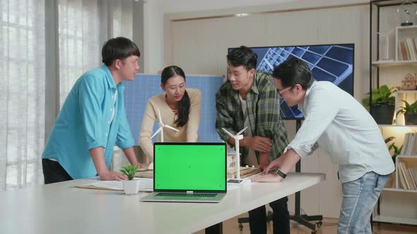 Green Screen Laptop On The Table While Asian Engineers Group Discussing House Model With Solar Panel alt