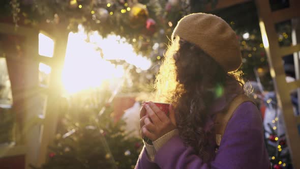 Positive Woman Drinks Beverage at Winter Fair at Sunset