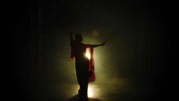 Silhouette a Young Girl Dancer in a Red Sari. Indian Folk Dance. Shot in a Dark Studio with Smoke alt
