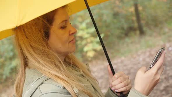 Young woman holding smart phone in the park and yellow umbrella female  slow-mo 1080p HD footage - S