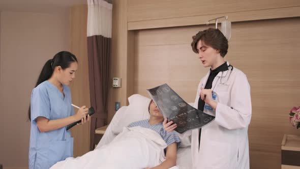 Female doctor explains x-ray film to patient at inpatient room bed in hospital.