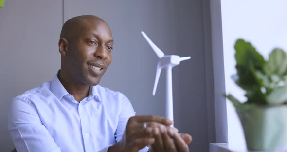 Businessman looking at wind turbine model in office alt