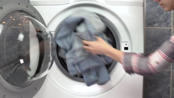 A Young Woman Is Actively Loading Clothes with a Washing Machine. The Woman Opens the Washing alt