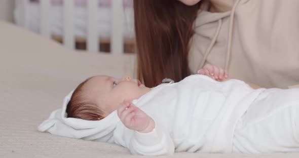 A Mother Leans Over Her Newborn Baby Lying On The Bed