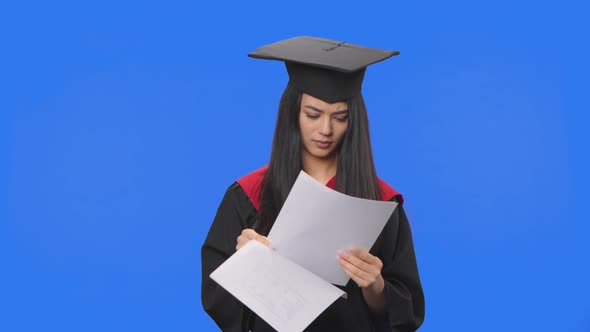 Portrait of Female Student in Graduation Costume Looking Through Documents Tearing Them Up and alt