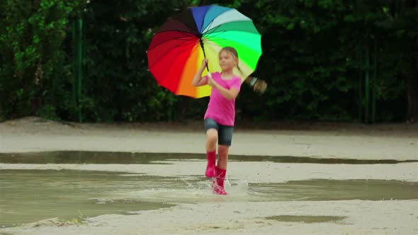 Happy funny ba child by girl with a multicolored umbrella jumping on puddles in rubber boots