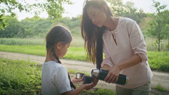Happy Asian Woman Enjoys Vacation with Her Daughter Walking Along the Forest Path Drinking Tea From