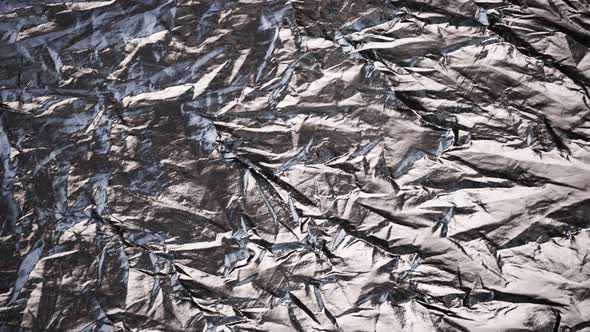 Crumpled, aluminium foil shining in the spotlight. Endless, abstract pattern. 4K