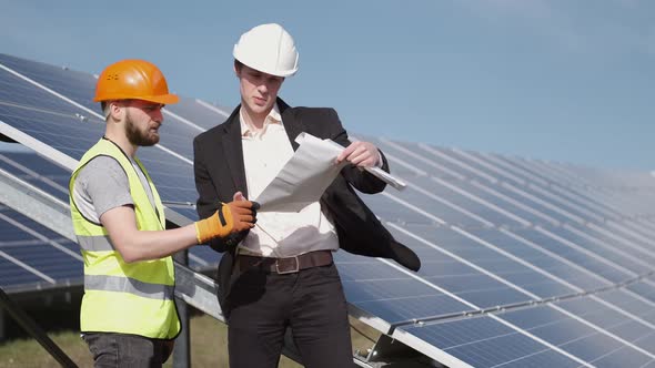 The Businessman and Worker Are Discussing Documents Standing Near Solar Batteries Outside alt