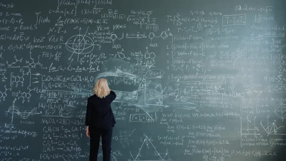 Smart Woman Researcher Walking To Blackboard in Classroom Writing Formulas alt