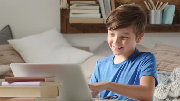 smiling student boy studying at home with remote school connected to computer on the web