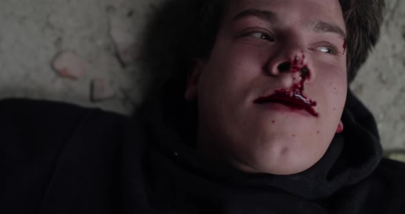 Close Portrait of a Wounded Bloodied Man Lies on a Floor Coughs and Suffocates alt