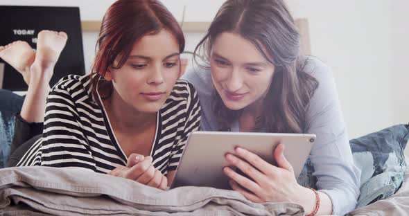 Two friends at home looking at digital tablet alt
