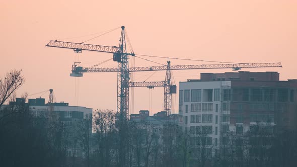 Dark Silhouette of Tower Cranes at High Residential Apartment Buildings Construction Site at Sunset alt