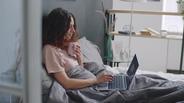 Woman Using Laptop and Drinking Coffee in Bed alt