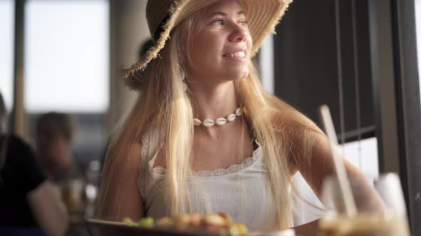 Female with Long Blonde Sitting in Cafe Looking Sideways Smiling alt