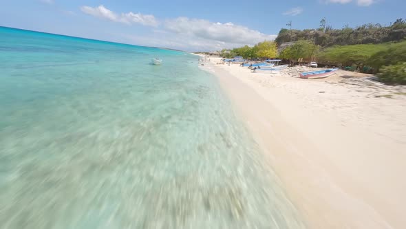 First person aerial racing drone pov over sandy beach with tourists and turquoise sea of Cabo Rojo i alt
