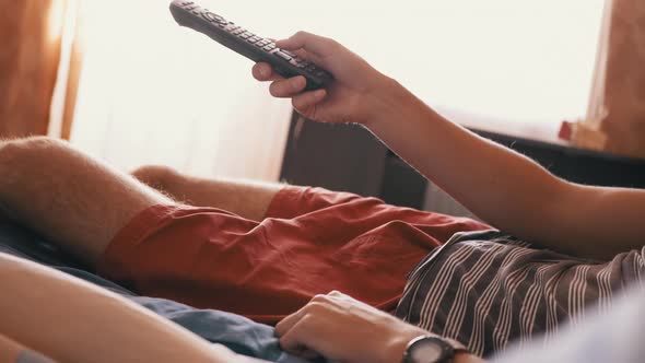 Tired Man Lies on the Bed and Emotionally Watches TV with Remote Control alt