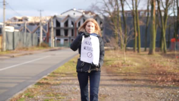 Slim Caucasian Woman with No Housing Needed Placard Walking to Camera Showing Message alt