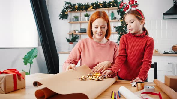 Zoom in Portrait of Happy Little Girl and Mother Wrapping Christmas Gifts Together at Home Trying alt