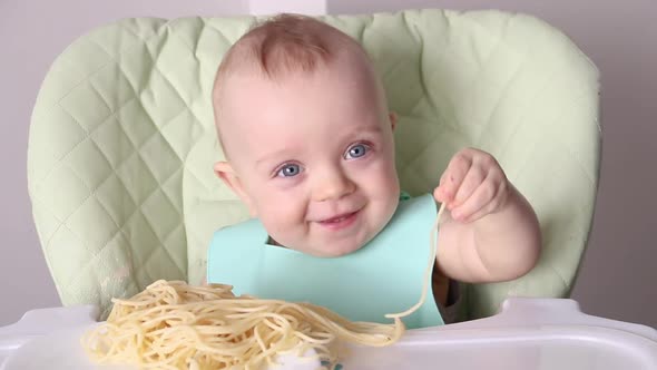 a Little Boy Touches Spaghetti with His Hands While Sitting in a Child's Chair alt
