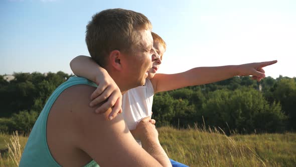 Redhaired Boy and His Father Sitting at Green Grass on the Lawn and Pointing at Something Outdoor alt