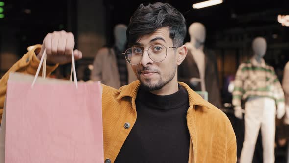 Stylish Joyful Young Guy Shopper Stands in Boutique Points to Packages Satisfied with Good Purchase alt