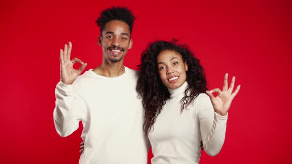 Young African Couple Making OK Sign Over Red Background. Winner. Success alt