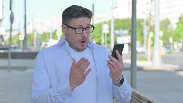 Upset Man Reacting to Loss on Smartphone Outdoor alt