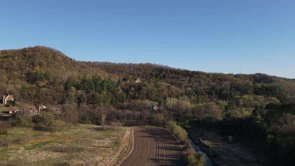 View up rural valley in Wisconsin. Meadow with plowed field near creek. Shrine tucked in trees.